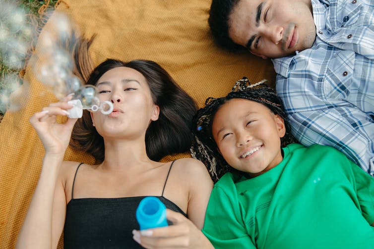 People seen lying on a blanket, one person blowing bubbles.