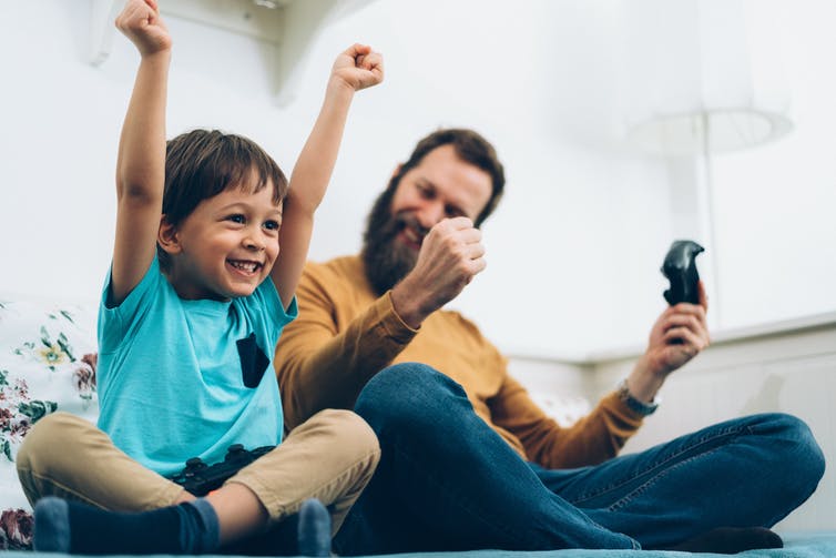 A father and son playing a video game together cheer in victory.