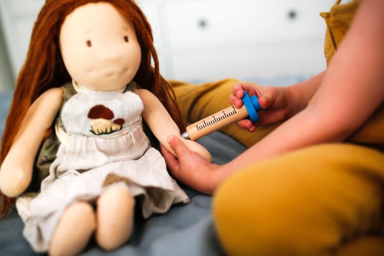 A child gives a doll a vaccine.