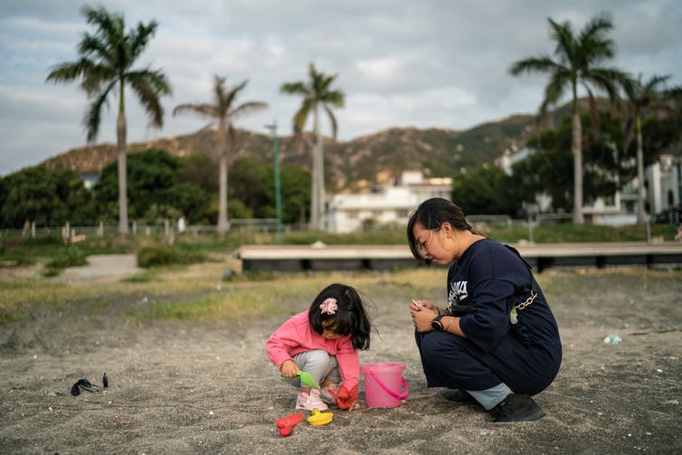 Mother plays with daughter in sand at beach