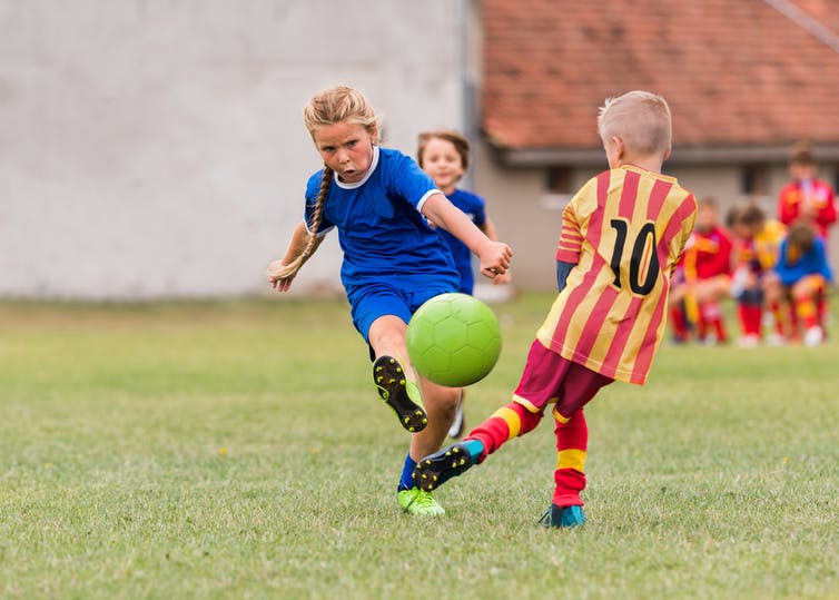 Girl in blue kicking football.