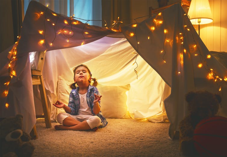 A girl meditates under a sheet covered in lights