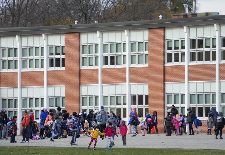 The front of a school is seen and children are walking out.