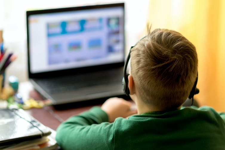 Photo from behind of a young boy using a computer while wearing a headset.