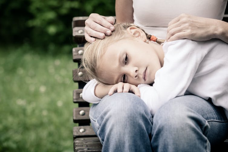 Child with head on mother's lap looking sad