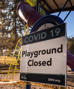 A sign attached to an outdoor play structure says 'COVID-19: Playground closed.'