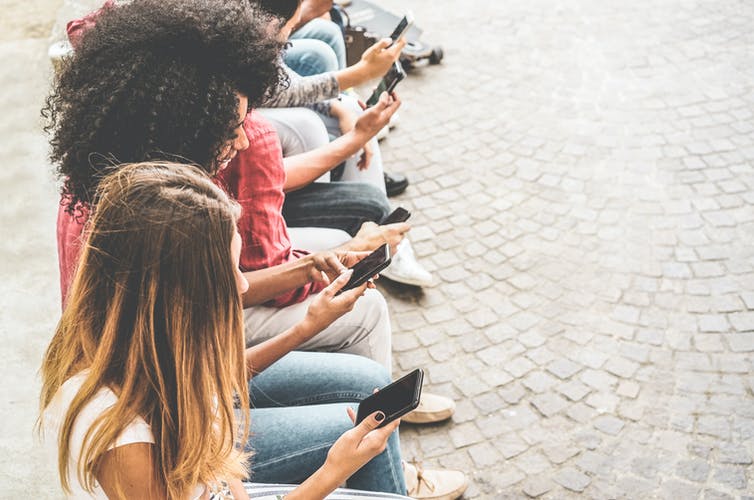 An overhead shot of women sitting in a row and looking at their phones.