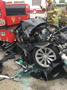 The crumpled front end of a wrecked car against the rear end of a fire engine