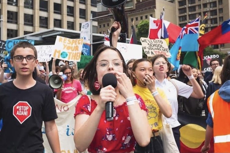 A phalanx of chanting students march toward the camera flanked by placards and flags.