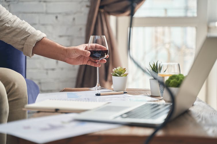 A hand reaches for a glass of wine on a coffee table.