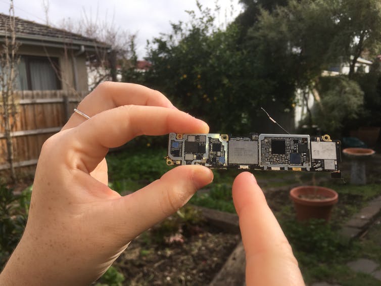 A hand holds the components of an iPhone 6S, pointing to a tiny chip.