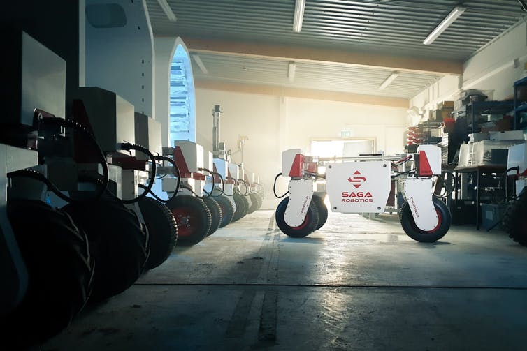 Four-wheeled robot in a garage next to a line of other robots