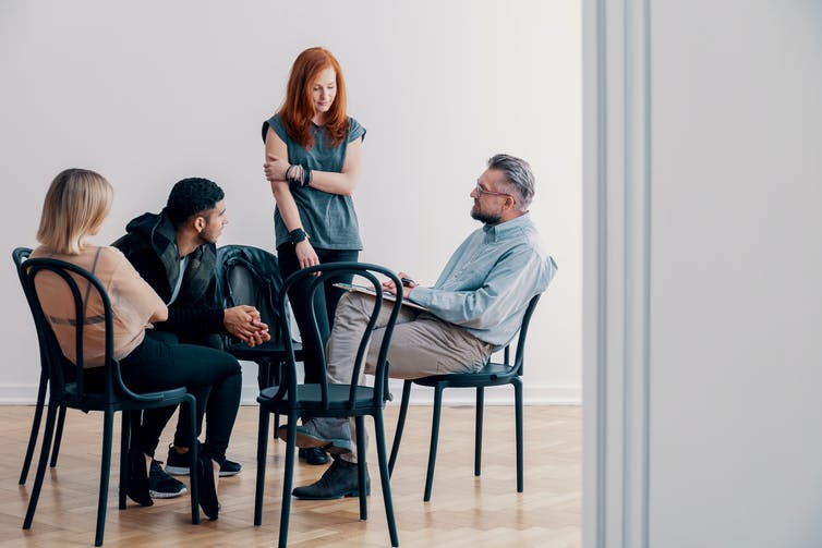 A group therapy session. One woman is standing and addressing three others.