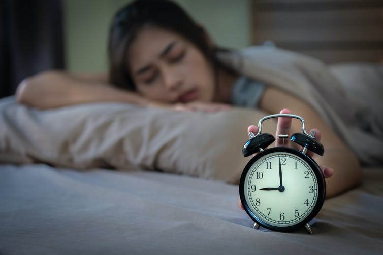 Teen girl waking up in bed and switching off alarm clock.