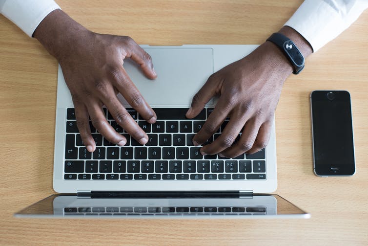 Birds-eye view of a man typing on a laptop. There is also a smartphone on the desk.