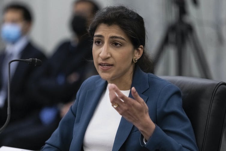 A seated woman gestures with her left hand as she speaks into a microphone