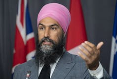 NDP Leader Jagmeet Singh responds to a question as he gestures and stands behind a podium.