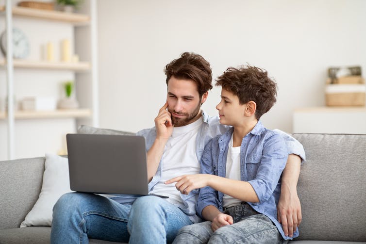 father and son seated on a couch discussing something on their laptop