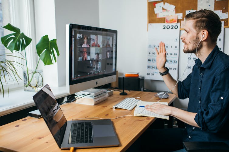 A man sits at a desk with a laptop and desktop computer