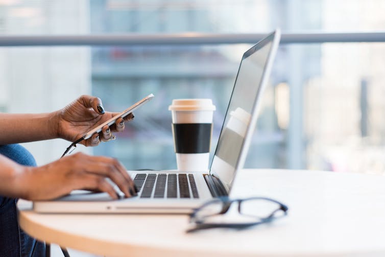 Hands using a laptop and smart phone at a desk