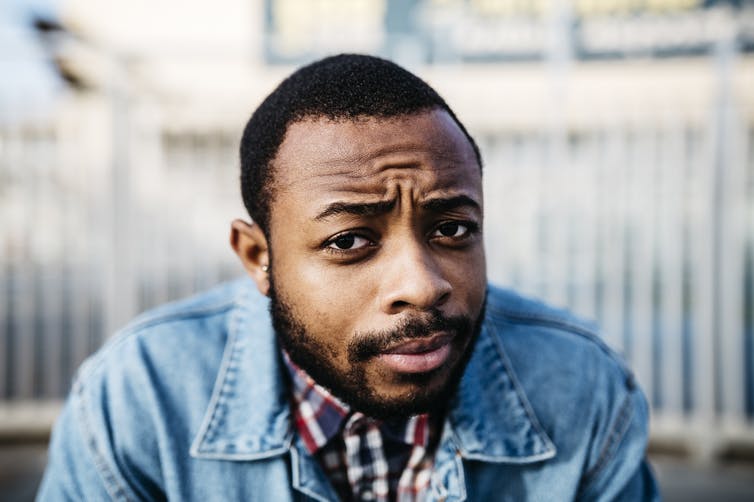 A man in a beard wearing a jean jacket looking quizzical.