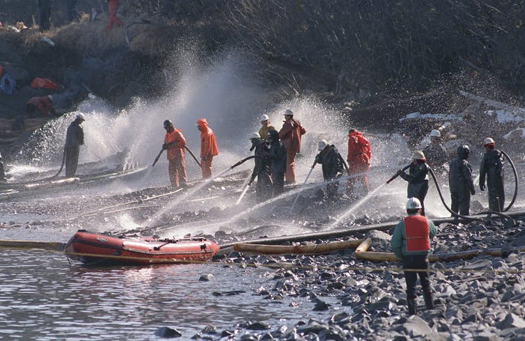 People are using high pressured hoses to wash oil from rocks on a beach.