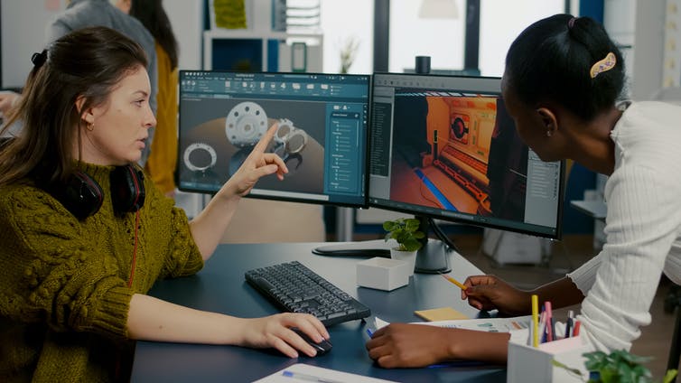 Two video game workers looking at a computer screen with an unfinished video game on it