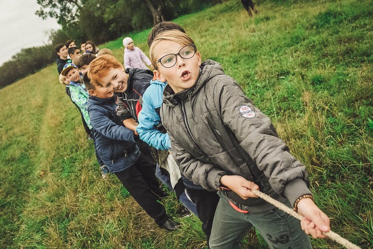 Young boys play tugowar in a green field.