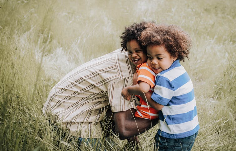 A parent with two young children in a field of long grass.