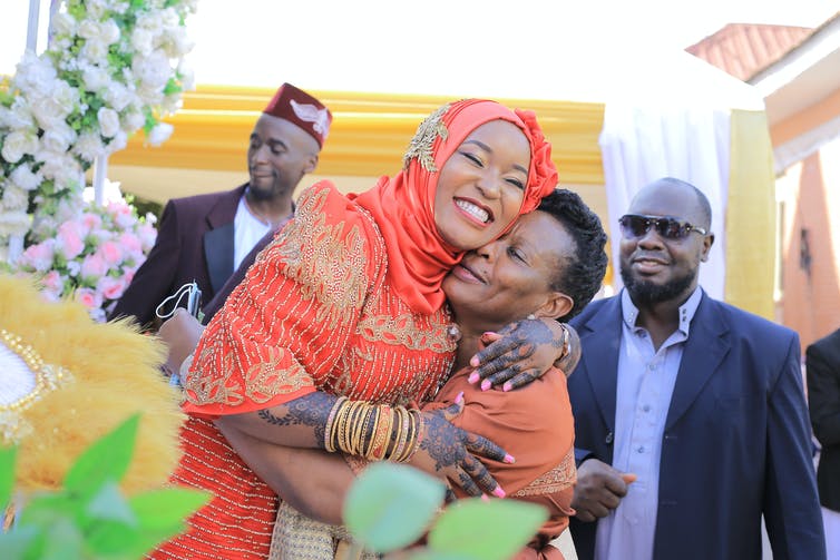 A bride in orange hugs her mother.