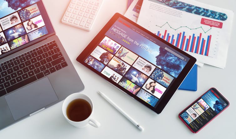 Laptop, tablet and phone showing a streaming platform, financial charts, coffee cup