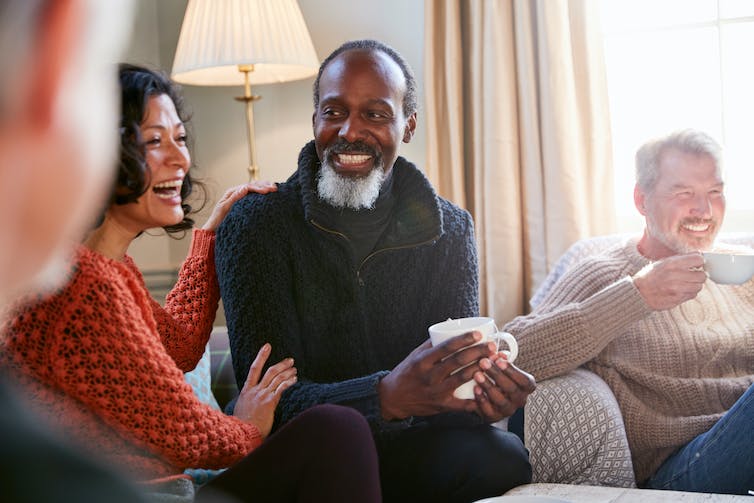 Four middle aged and older friends sitting in a living room and smiling with each other