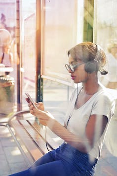 A teen sitting in glasses looking at a phone on a bus.