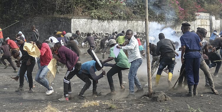 Police and protesters fight in a city street. Smoke is visible.