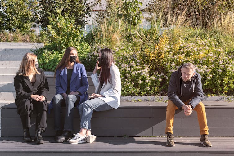 A group of women wearing masks talking, alongside a man not wearing a mask.