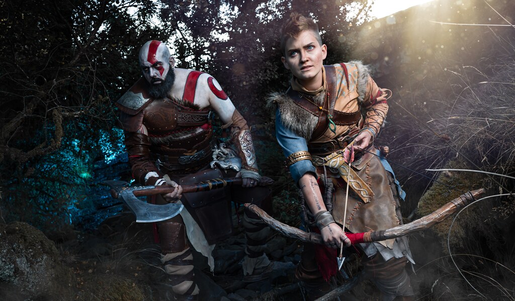 This image shows cosplayers portraying Kratos and Atreus emerging from a forest. Kratos They look ready for battle with their weapons drawn.