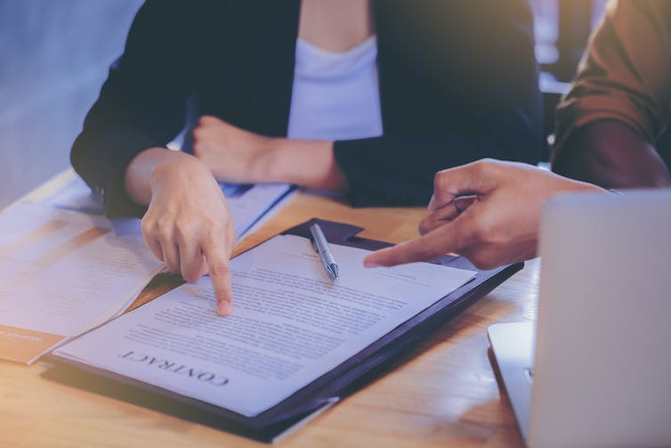 Two people in discussions about and pointing at a contract on a desk in front of them.