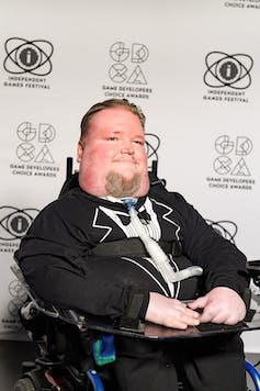 Steven Spohn wears a tuxedo in his wheelchair on the red carpet of the Game Developers Conference