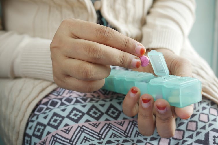 Hands taking pills out of a container.