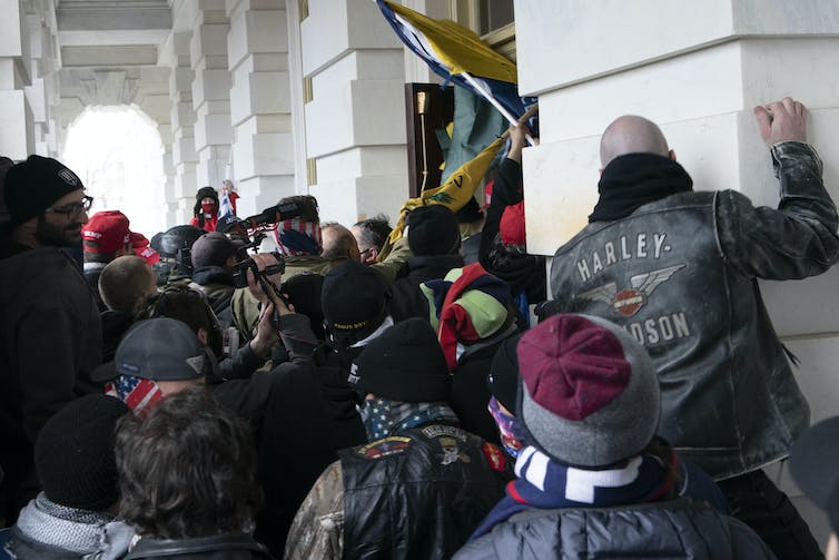 People in masks and hats move through a doorway.