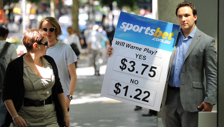 Man in suit holds sign advertising betting odds to passersby.