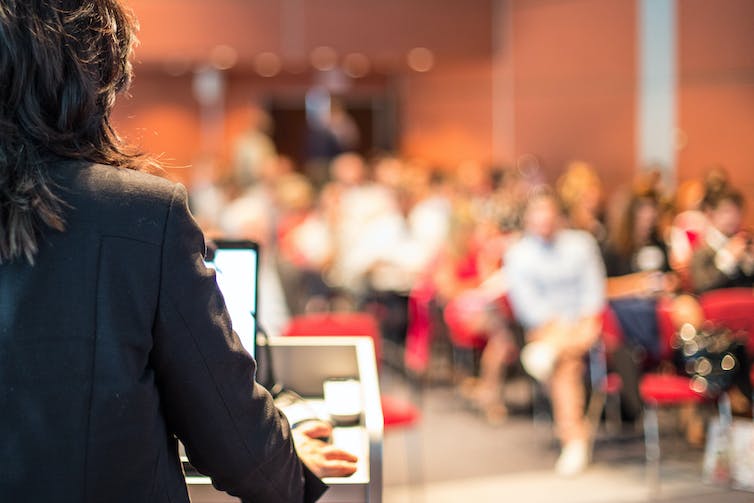 A woman gives a speech to a small auditorium.