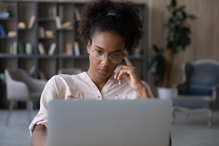 Woman looks at laptop; home in background; remote working.