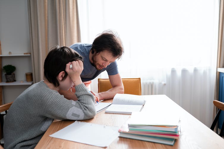 A dad leans over his son's work.