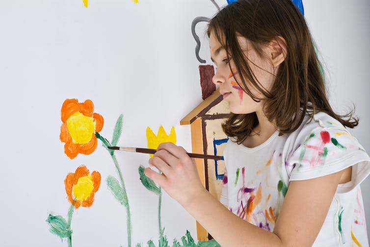 A child paints a flower on a wall.