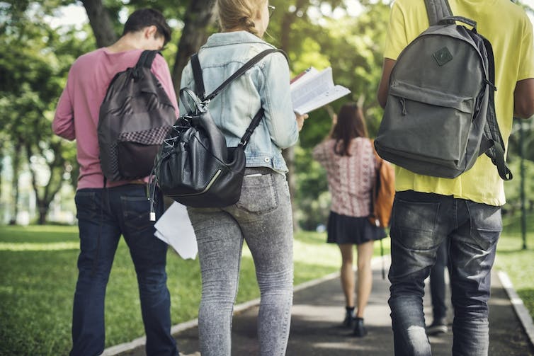 Young people wearing backpacks seen from behind.