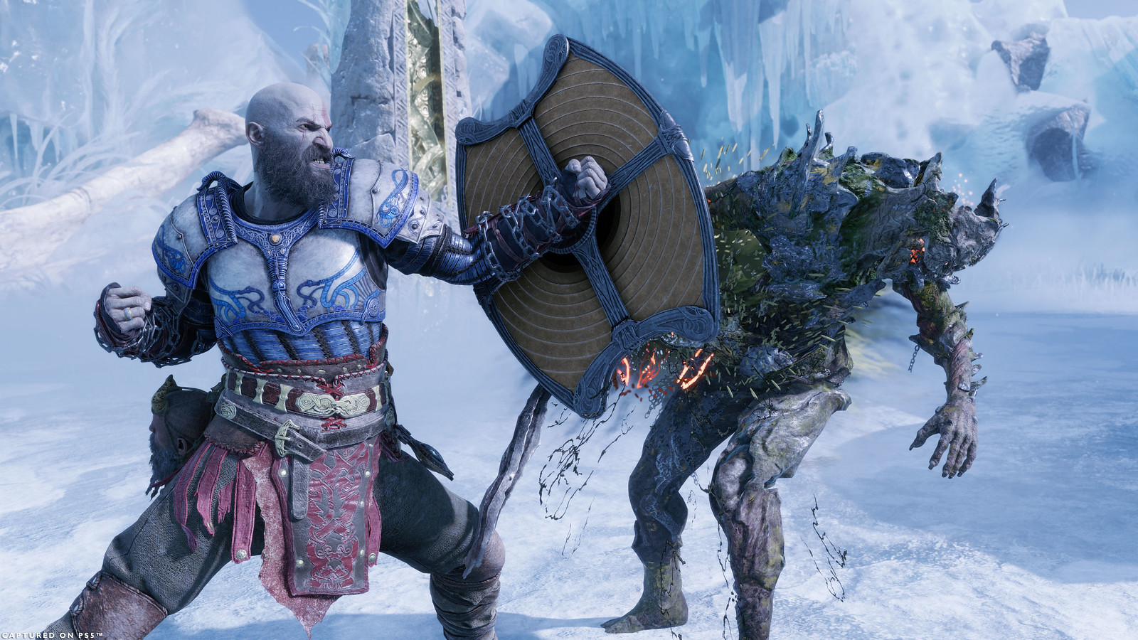 Kratos strikes out against a Draugr with his shield, the attack inflicting Poison against it. They are fighting in the Niflheim Arena, the ground and walls are covered in ice. Kratos is wearing the equipment from the build.