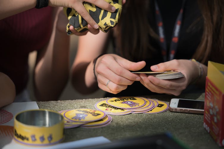 A pair of hands holds a collection of round cards. There is another pile of round cards on the table beneath the hands.