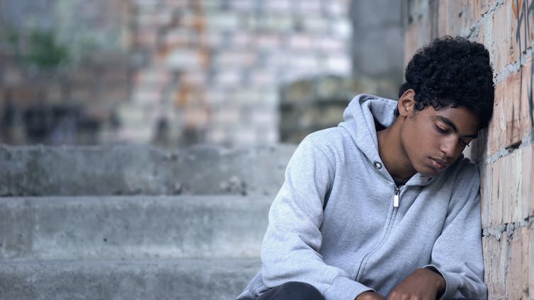 A young sad-looking boy leans his head on a wall.