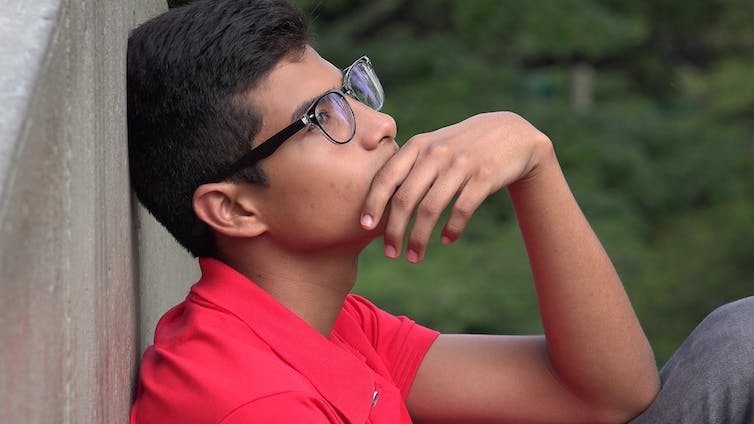 Pensive teenage boy in glasses sat with back to wall